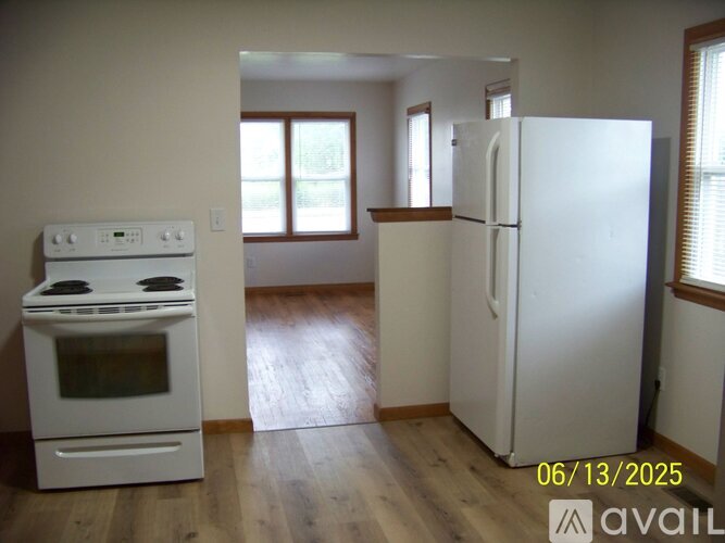 A kitchen with a white stove and refrigerator in a room with wood floors and white walls.