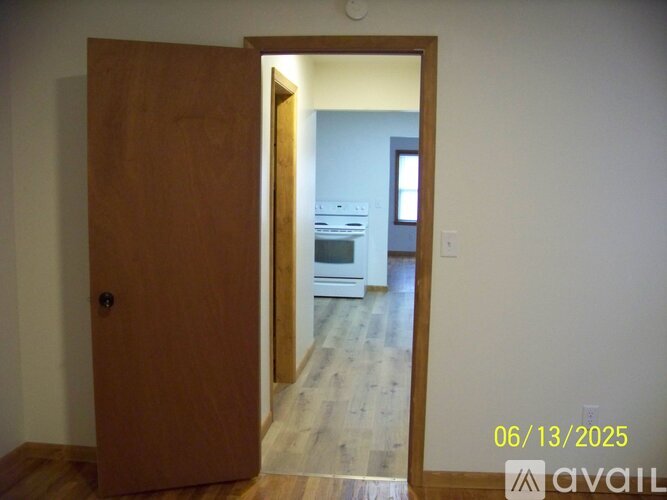 A wooden door opens to a kitchen with white appliances.