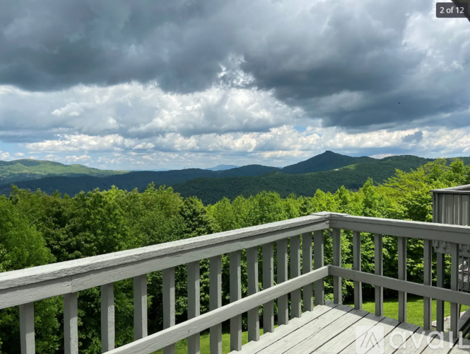 A wooden deck overlooks a mountain range under a cloudy sky.