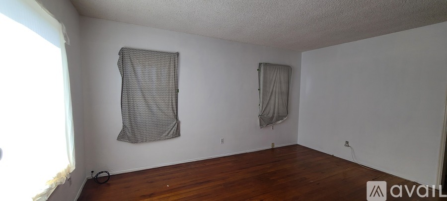 A room with wooden floors and two windows covered with curtains.