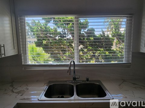 A kitchen with a double sink and a window with blinds.