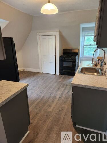 A kitchen with a black fridge, a white door, a black oven, and a wooden floor.