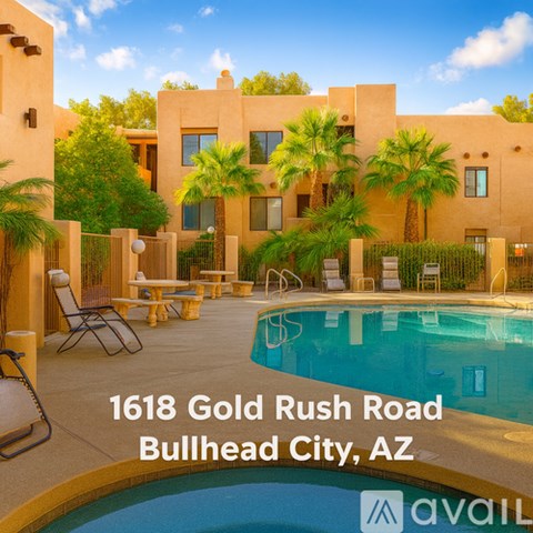 A pool and lounge chairs are in front of a tan building with palm trees in the background.