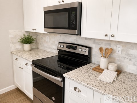 A kitchen with a black microwave above a stove and white cabinets.