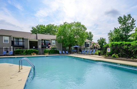 A swimming pool in front of a building with trees and chairs around it.