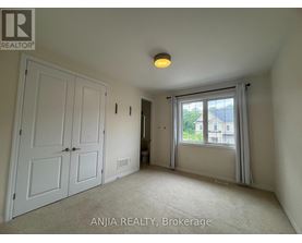 A room with a carpeted floor, a ceiling light, and a window with a view of a building outside.
