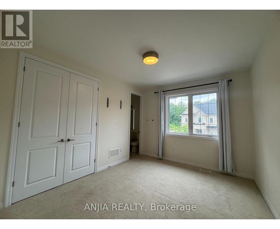 A room with a carpeted floor, a ceiling light, and a window with a view of a building outside.