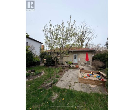 A backyard with a tree, a swing set, and a red umbrella.