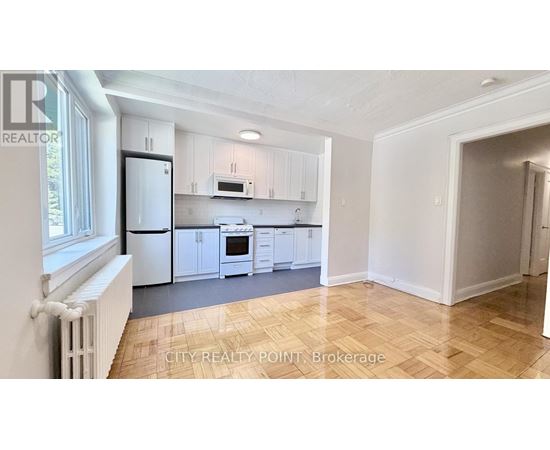 A kitchen with white cabinets and appliances in a room with wooden flooring.