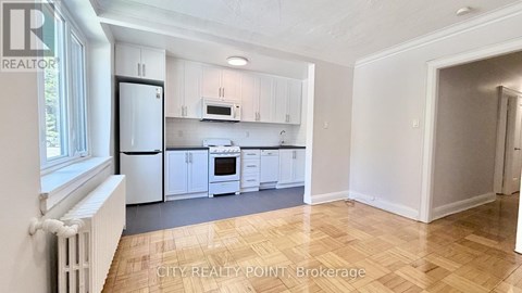 A kitchen with white cabinets and appliances in a room with wooden flooring.