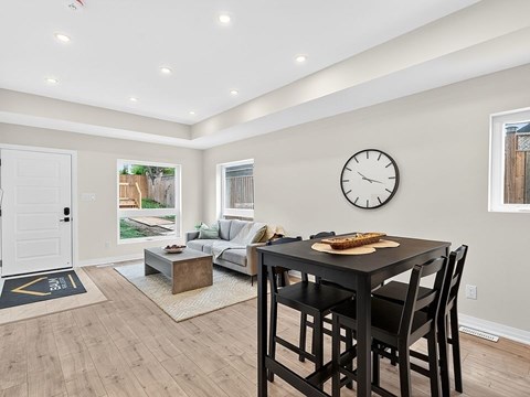 A black dining table with four chairs is in the center of a room with a clock on the wall.