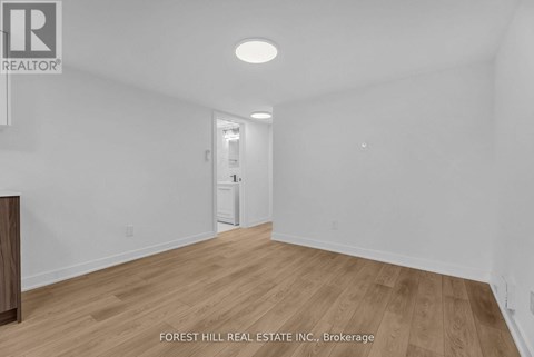 A room with wooden flooring and white walls, with a door at the end.