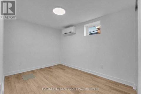 A room with a window, a wall-mounted air conditioner, and a wooden floor.