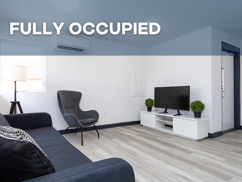 A living room with a grey sofa, a black chair, and a television on a white stand.