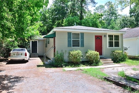 A house with a red door is surrounded by greenery.