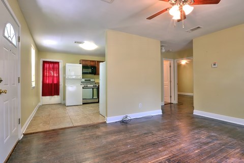 A room with a ceiling fan and a kitchen area in the background.