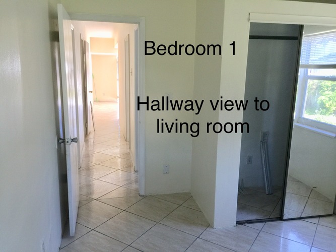 A hallway view to a living room with Bedroom 1 at the end.