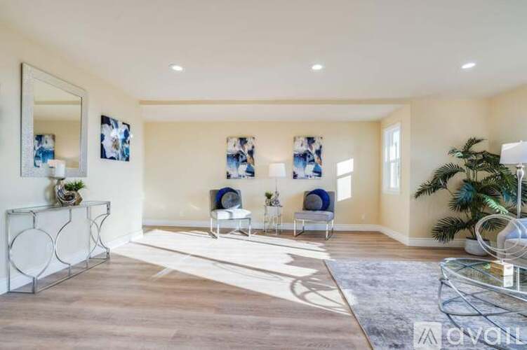 A spacious living room with a white sofa set and a glass coffee table.