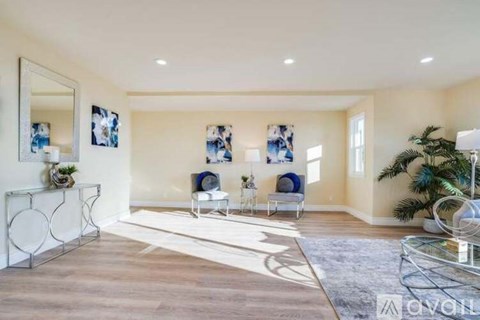 A spacious living room with a white sofa set and a glass coffee table.