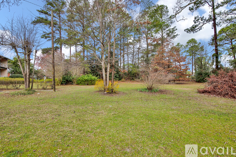 A grassy field with trees and a house in the background.