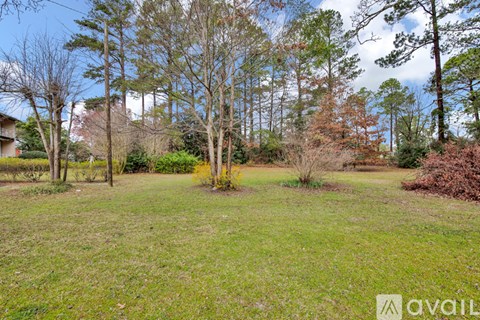 A grassy field with trees and a house in the background.