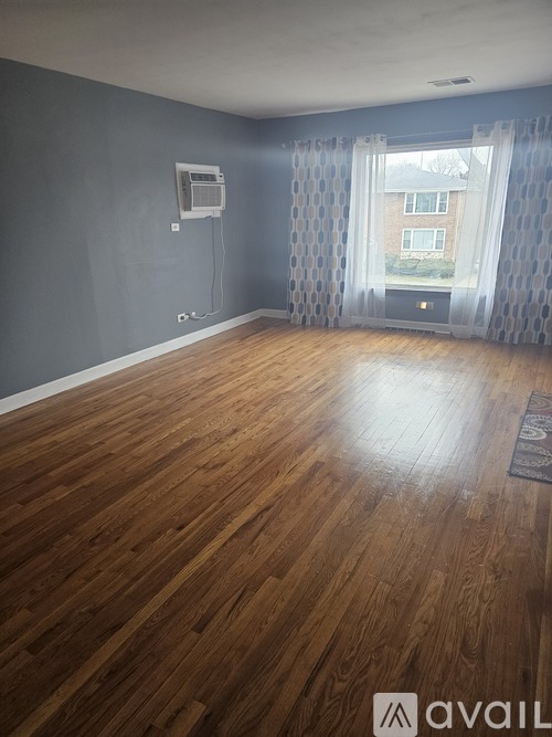 A room with wooden flooring and a window with curtains.