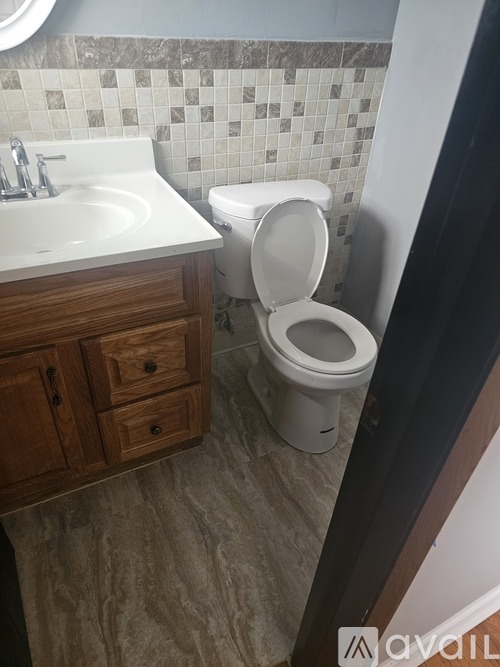 A white toilet is in a bathroom with a white sink and wooden cabinets.