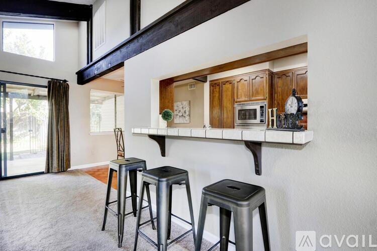 A kitchen area with a bar stool and a countertop with a microwave and clock.