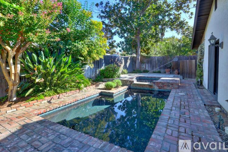 A backyard with a pool and a brick walkway.