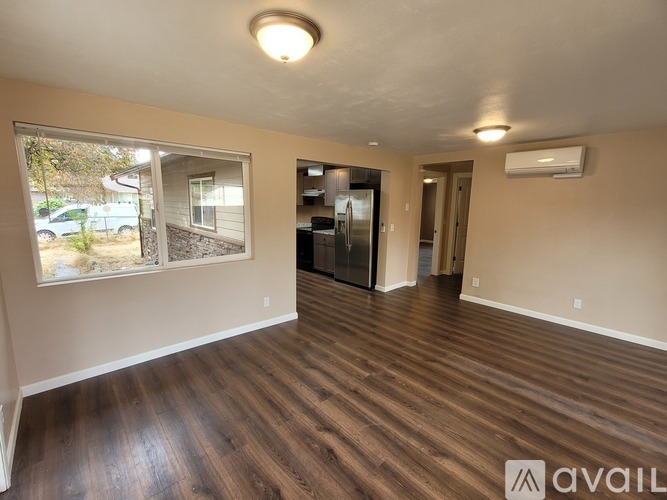 A room with wooden floors and a window showing a view of a house and trees.