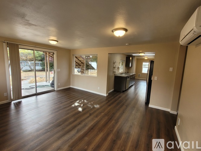 A spacious room with wooden floors and sliding glass doors leading to a backyard.