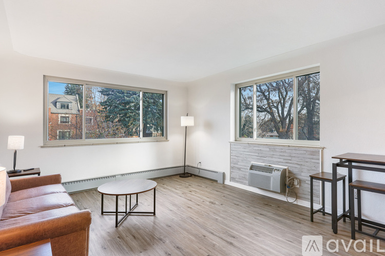 A living room with a brown leather couch, a white coffee table, and a large window with a view of a house and trees.