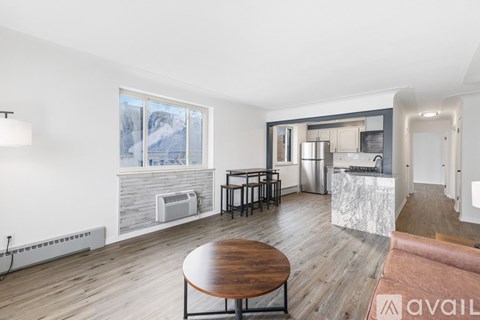A modern living room with a wooden table and chairs, a kitchen area with stainless steel appliances, and a view of snowy mountains through the window.