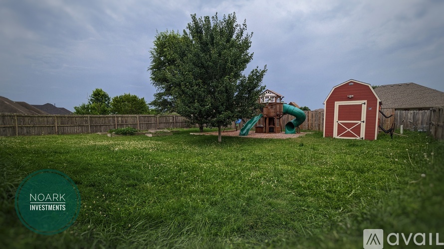 A red barn sits in a grassy field with a slide in the background.