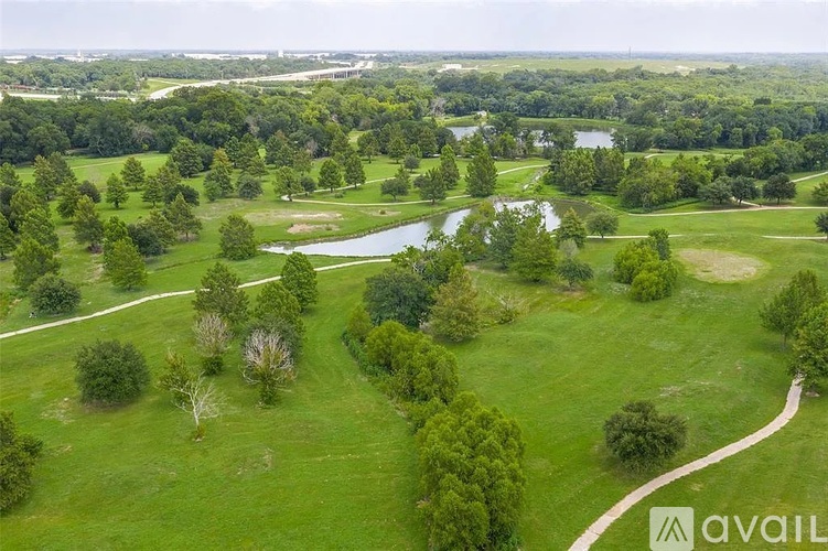 A large grassy field with a winding path and a lake.
