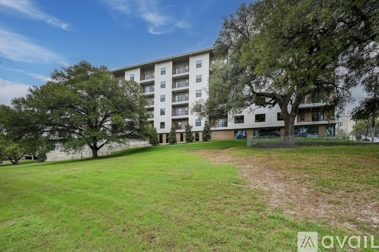 A large grassy area in front of a multi-story building with trees.