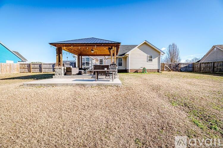 A house with a covered patio is surrounded by a fence and a grassy area.