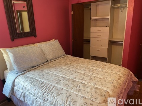 A bed with a white comforter and two pillows sits in a room with red walls.