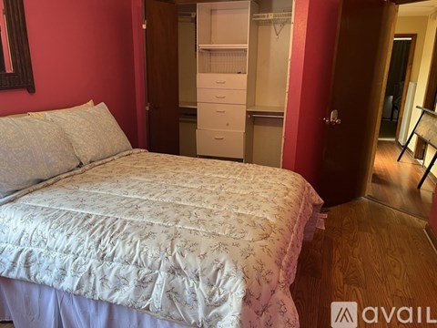 A bed with a white comforter is in the foreground of a room with red walls.