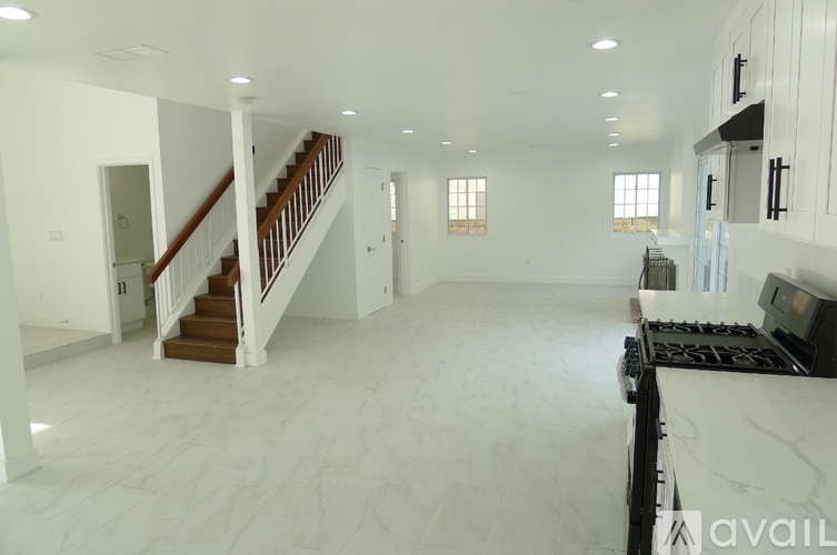 A spacious, empty living room with a staircase and a kitchen area.