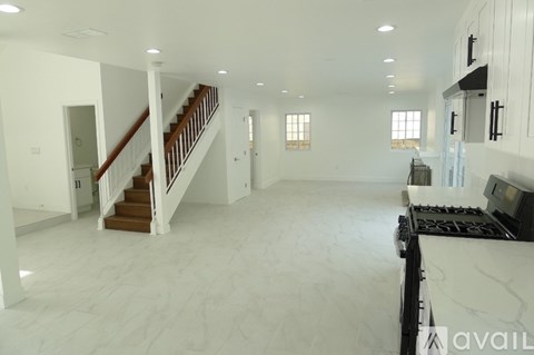 A spacious, empty living room with a staircase and a kitchen area.