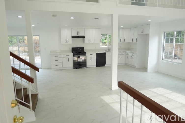 A large, empty, white kitchen with a stove top oven and a refrigerator.
