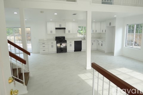 A large, empty, white kitchen with a stove top oven and a refrigerator.