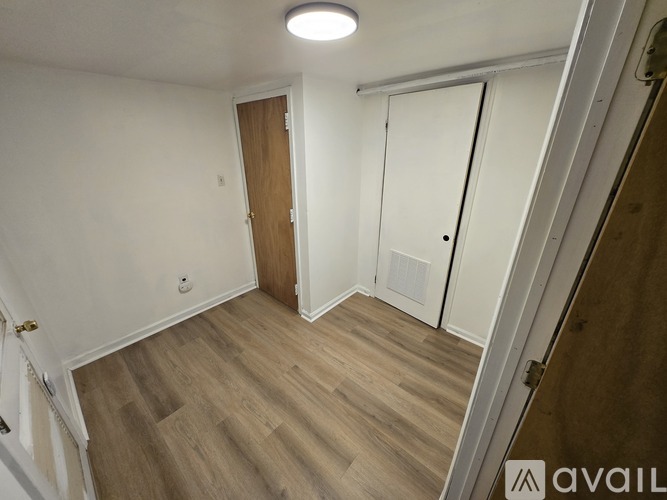 A room with a wooden floor and a white wall with a door and a cabinet.