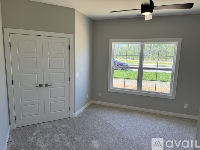 A room with a white door and a window with a view of a car and trees outside.