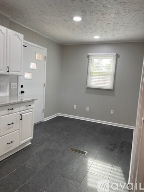 A kitchen with white cabinets and a window with blinds.