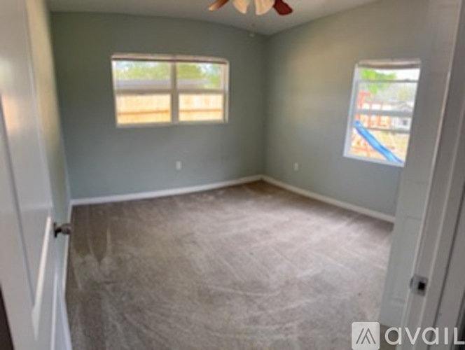 A room with a carpeted floor and two windows.