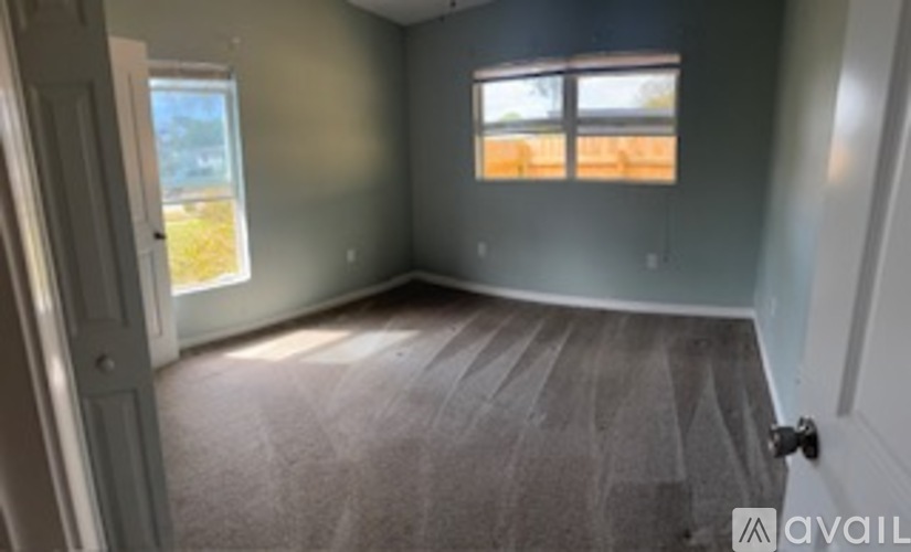 A room with a carpeted floor and a window with a view of a field.