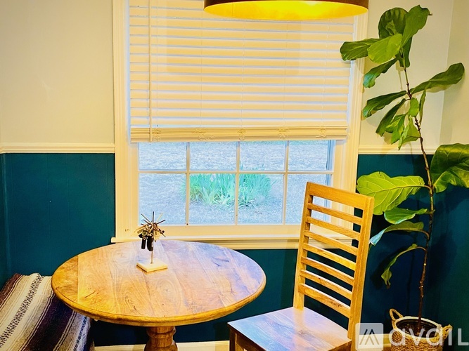 A wooden chair sits next to a round wooden table with a lamp on top.