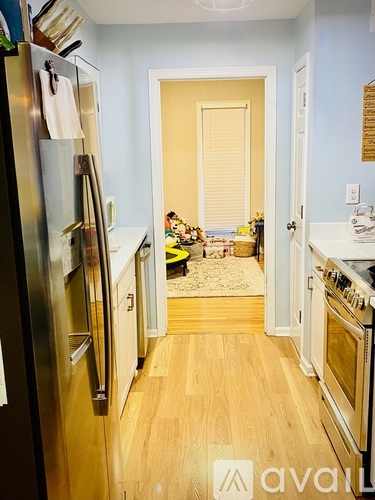 A kitchen with wooden floors and a refrigerator on the left.
